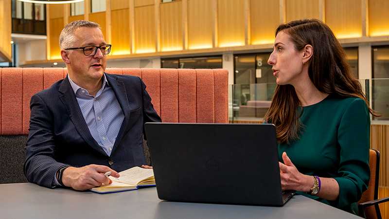 Two people talking a a desk with a laptop